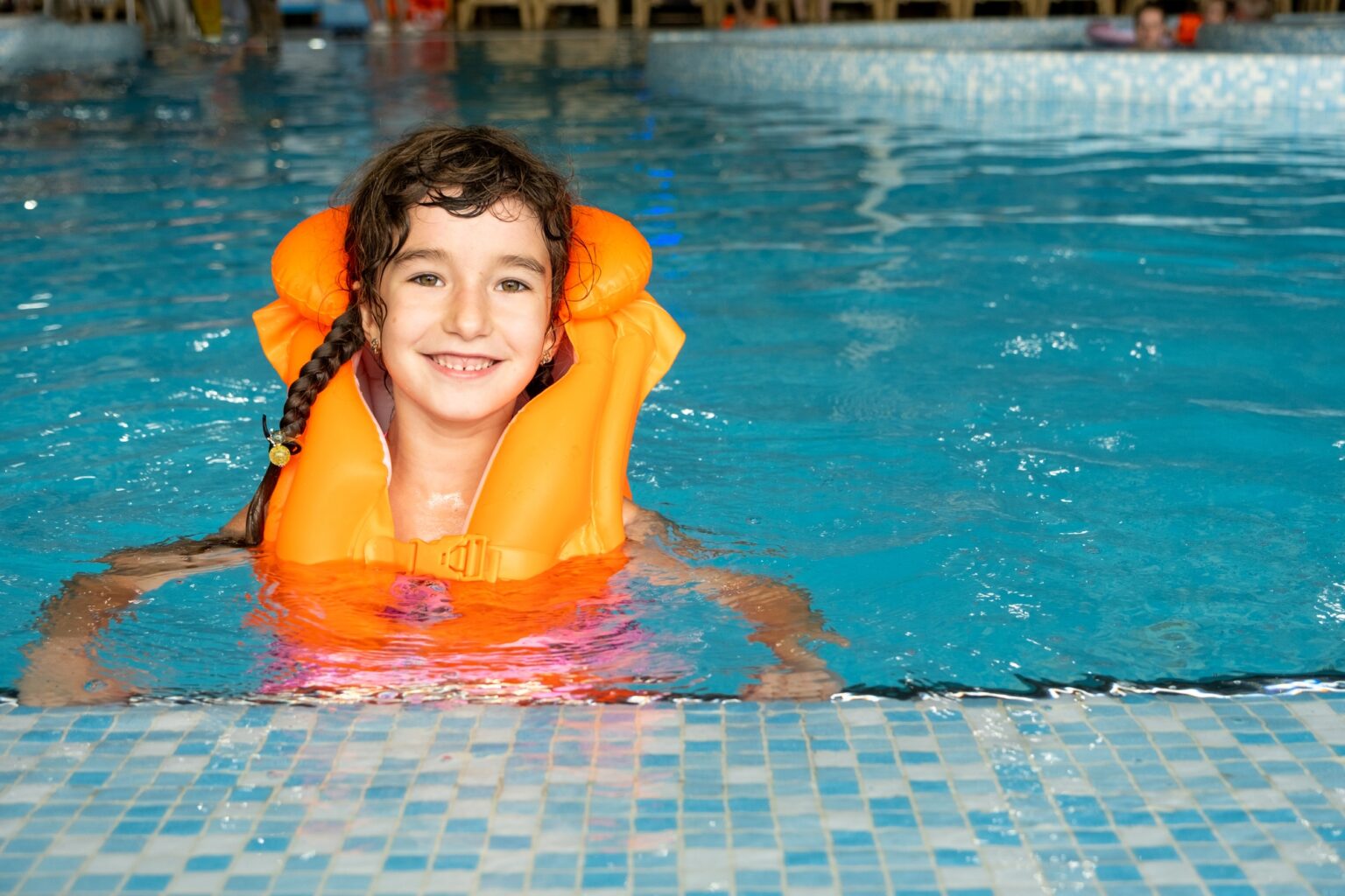 Pediatric Drowning Prevention: Safeguarding Our Most Valuable Assets A child in an orange life jacket swims in the pool in an aqua complex