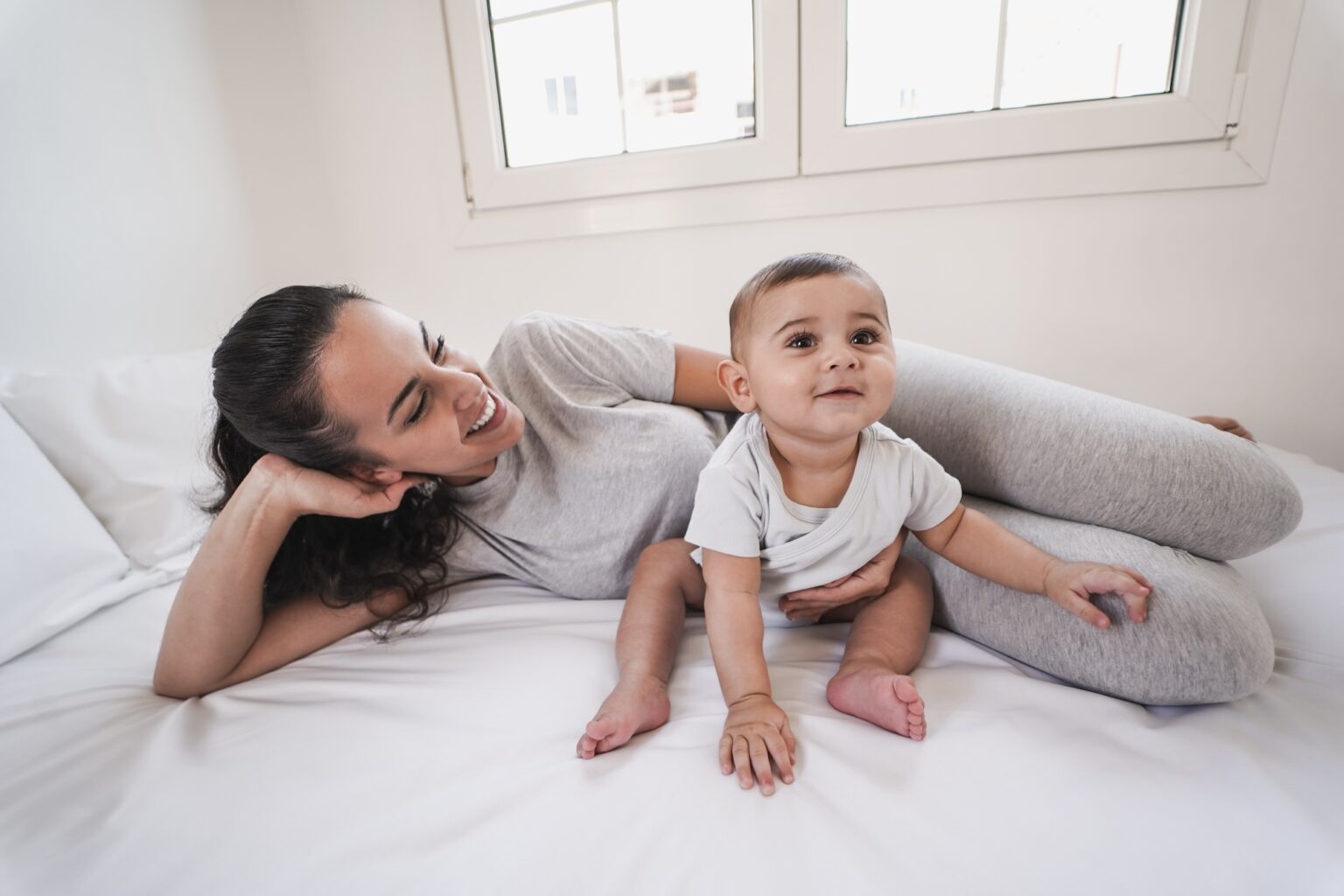 Young loving mom lying on bed with her 6 months old baby at home - Mother and toddler love