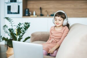 A smiling 5-6 years old girl watching a laptop screen, sitting on a beige couch