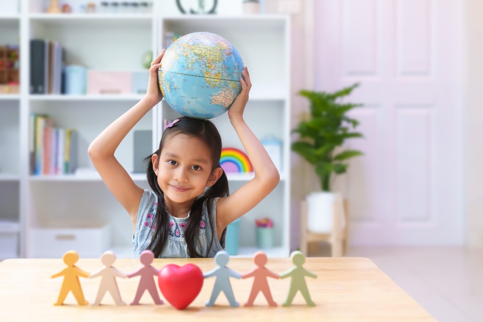 Asian little girl smiling and put bilingual globe on head behind heart model.